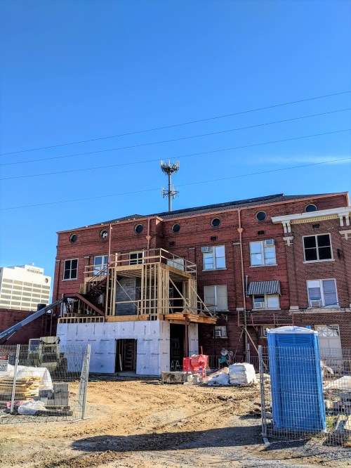 Construction site of a brick building with scaffolding, a cell tower, and construction materials in the foreground.