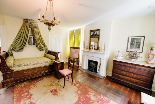 A vintage room featuring a daybed with drapery, a fireplace, wooden furniture, and floral decor.