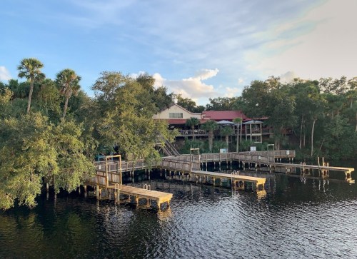 A serene waterfront scene featuring wooden docks and lush greenery under a blue sky with scattered clouds.
