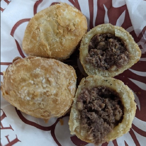 A close-up of golden-brown pastries, some whole and one cut open, revealing a savory meat filling inside.