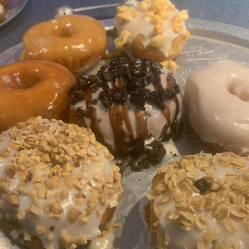 A platter of assorted donuts, including glazed, chocolate, and topped with popcorn and granola.