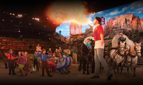 A lively stage performance featuring actors, horses, and special effects in a colorful Western-themed setting.