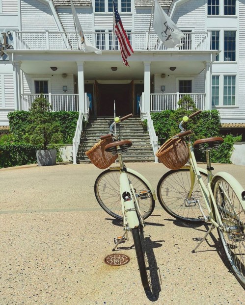 Two bicycles with wicker baskets parked in front of a white building with flags and greenery.