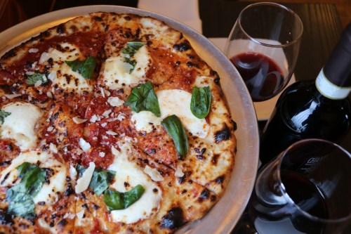 A delicious pizza topped with mozzarella, basil, and tomato sauce, accompanied by two glasses of red wine.