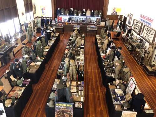 Aerial view of a museum exhibit featuring military uniforms, artifacts, and historical displays on tables.
