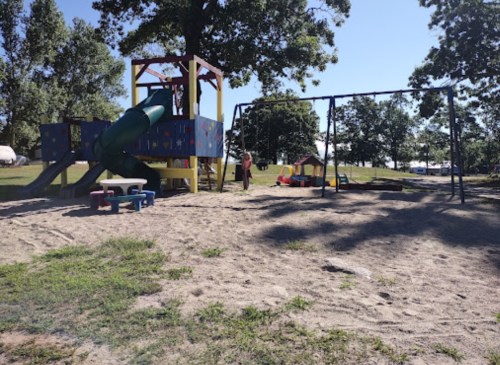 A colorful playground with a slide, swings, and play structures, set in a sandy area under clear blue skies.