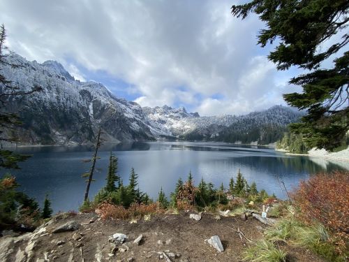 A serene lake surrounded by snow-capped mountains and evergreen trees under a partly cloudy sky.