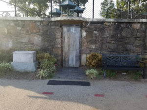 A weathered wooden door set into a stone wall, with a bench and a small stone structure nearby.