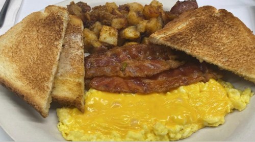 A plate of breakfast featuring scrambled eggs with cheese, crispy bacon, golden hash browns, and toasted bread.