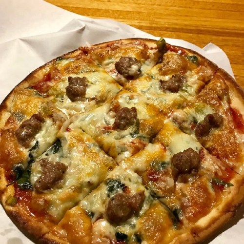 A freshly baked pizza topped with cheese, sausage, and spinach, cut into slices on a white paper.
