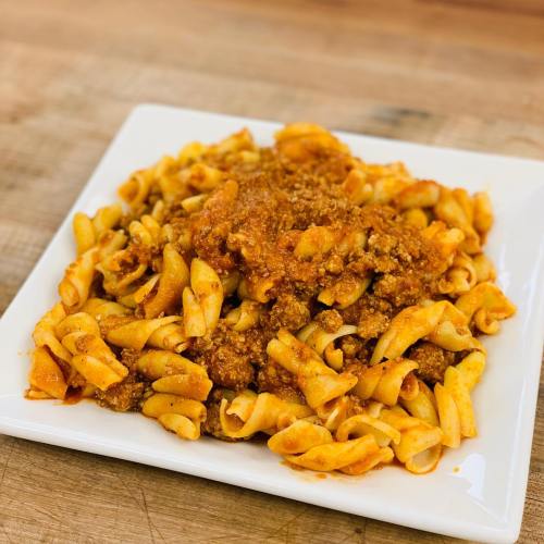 A plate of pasta with a rich meat sauce, served on a white square dish.