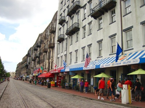 A lively street scene with shops, flags, and people enjoying the outdoors along a cobblestone path.