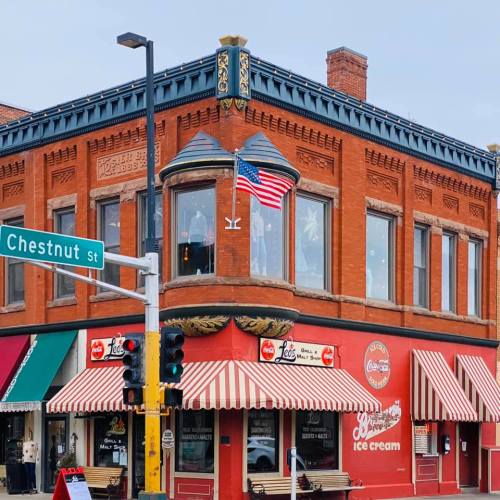 Historic brick building with an American flag, featuring striped awnings and a corner ice cream shop.
