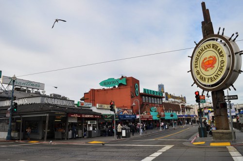 A bustling street scene at Fisherman's Wharf in San Francisco, featuring shops and a prominent sign.