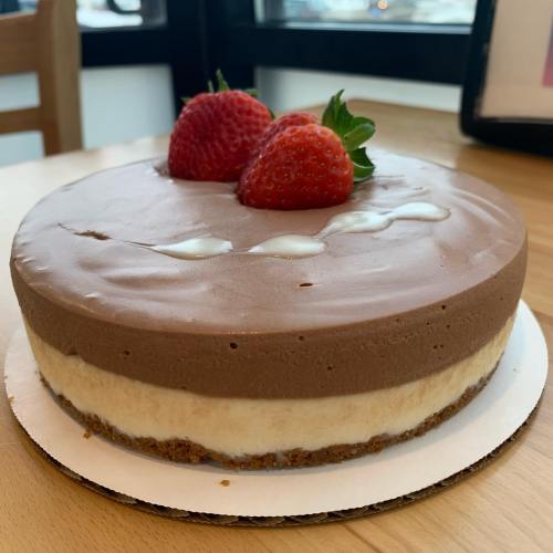 A round chocolate and vanilla cheesecake topped with two strawberries, sitting on a wooden table.