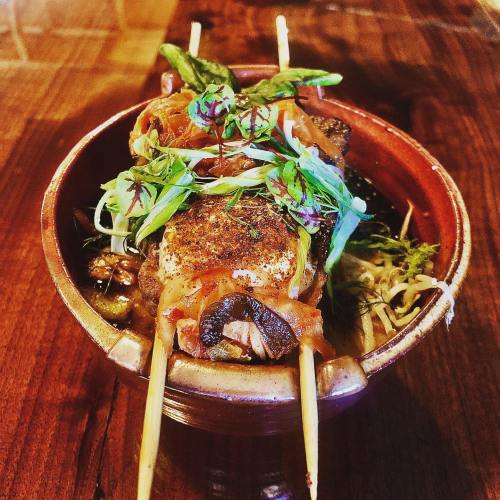 A bowl of skewered grilled meat topped with fresh herbs and vegetables, served in a rich broth.