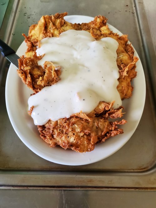 A plate of crispy fried chicken topped with creamy white gravy.