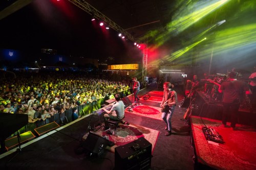 A lively concert scene with a band performing on stage in front of a large, enthusiastic crowd under colorful lights.