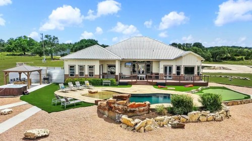 A spacious modern home with a pool, surrounded by landscaped grounds and a clear blue sky.