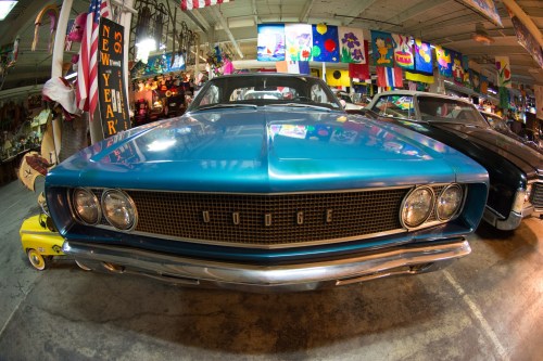 A vintage blue Dodge car displayed in a colorful, eclectic museum filled with various decorations and flags.