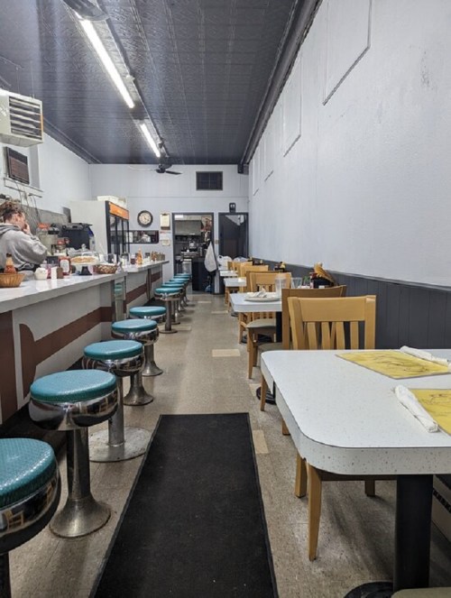 A diner interior with teal stools, white tables, and a long counter, featuring a cozy, retro atmosphere.