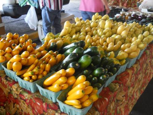 A colorful display of yellow and green squash arranged in baskets at a farmers market.