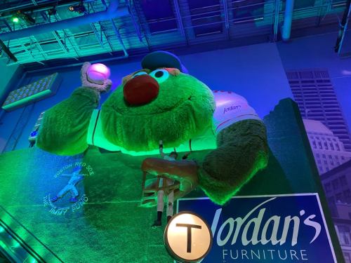 A large, colorful mascot holding a baseball, illuminated in green light, displayed at Jordan's Furniture.