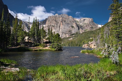 A serene mountain lake surrounded by lush greenery and towering peaks under a clear blue sky.