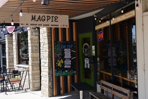 Exterior of Magpie café with a sign, outdoor seating, and a menu board displaying food and drink options.