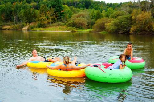 Four people relax on colorful inner tubes in a calm river, surrounded by trees and greenery.