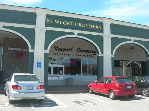 Exterior of Newport Creamery featuring ice cream and sandwiches, with parked cars in front and a clear blue sky.