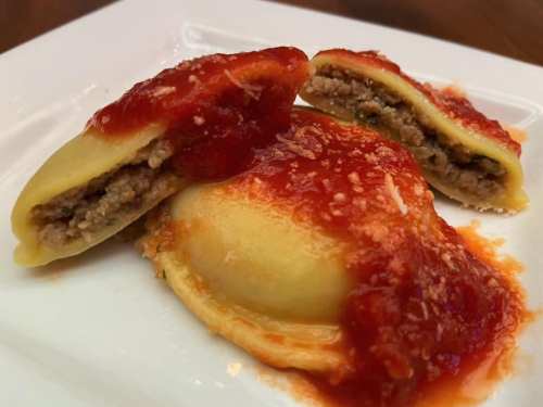 Three stuffed pasta pieces topped with marinara sauce and grated cheese on a white plate.
