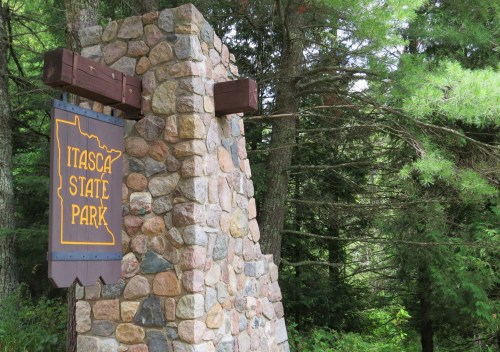 Stone sign for Itasca State Park surrounded by lush green trees.