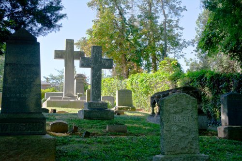 A serene cemetery scene featuring several gravestones and crosses surrounded by trees and greenery.