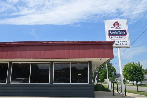 Exterior of Family Table Restaurant with a sign reading "Serving Fancy Good Food!" on a sunny day.