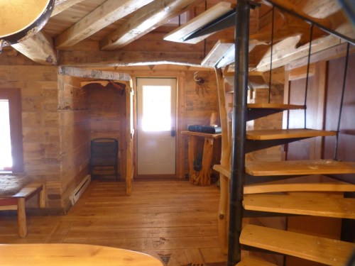 Cozy wooden interior with a spiral staircase, door to the outside, and rustic furniture. Warm, inviting atmosphere.