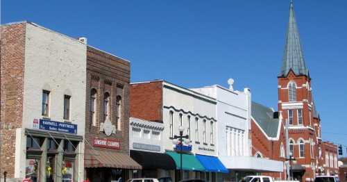 A row of historic buildings with shops and a church steeple against a clear blue sky.