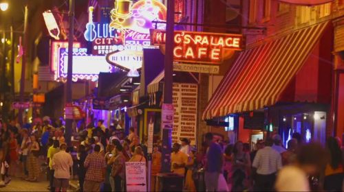 A vibrant street scene at night, filled with neon signs, bustling crowds, and lively cafes.