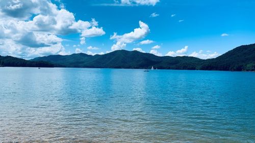 A serene lake surrounded by mountains under a bright blue sky with fluffy clouds.