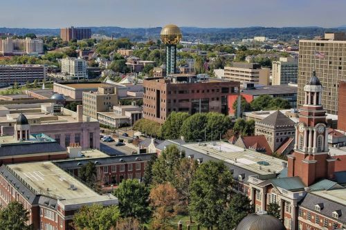 Aerial view of a cityscape featuring buildings, trees, and a prominent gold-domed structure in the background.