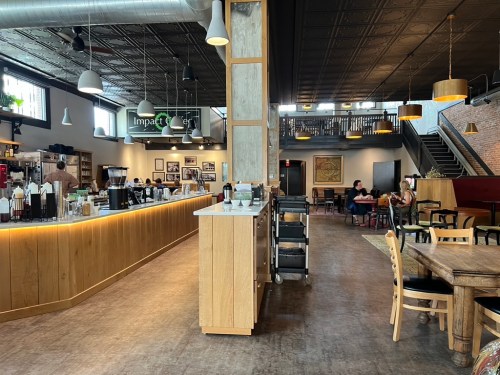 A modern café interior with a wooden counter, seating areas, and a staircase, featuring patrons enjoying their time.
