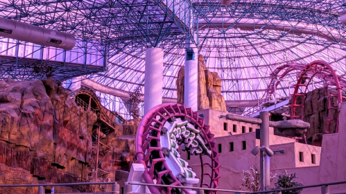Indoor amusement park featuring roller coasters, rock formations, and a large glass dome ceiling.