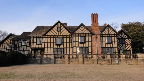 A large, historic Tudor-style house with black and white timber framing and a brick chimney, set against a clear sky.