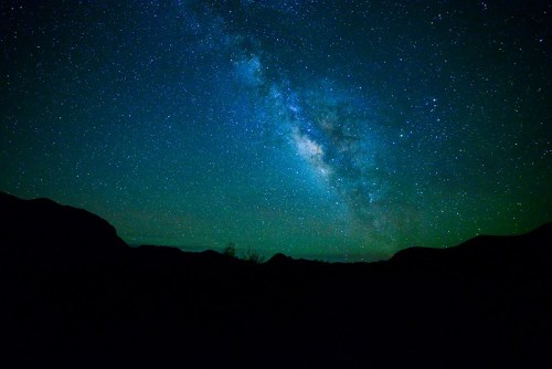 A stunning view of the Milky Way galaxy shining brightly in a star-filled night sky, silhouetted by dark mountains.
