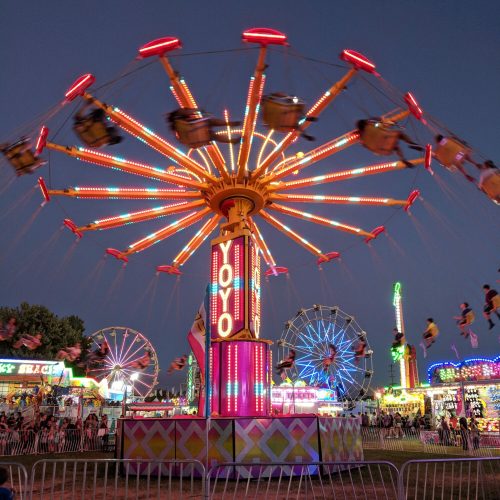 A vibrant carnival scene at night featuring a colorful swing ride and illuminated attractions in the background.