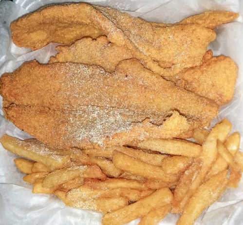 A serving of golden-brown fried fish fillets with a side of crispy French fries on a white paper background.