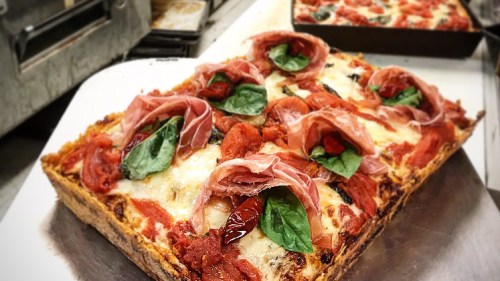A freshly baked pizza topped with slices of prosciutto, fresh basil, and tomato sauce on a golden crust.