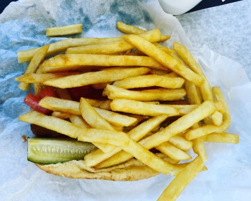 A hot dog topped with pickles and tomatoes, surrounded by a generous serving of golden French fries.