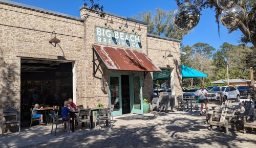 Exterior of Big Beach Brewing Co. with a rustic brick facade, outdoor seating, and disco balls hanging above.
