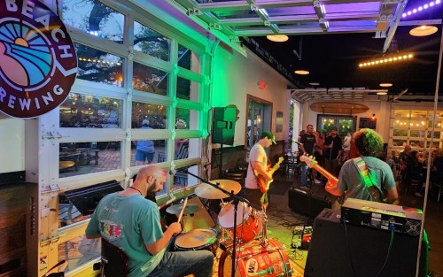 A live band performs inside a brewery, with colorful lights and an audience enjoying the music.